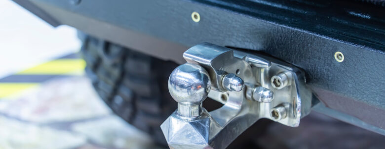 Close-up of a shiny metal tow hitch mounted on the rear bumper of a pickup truck rental in Highland, with part of a tire and ground visible in the background.