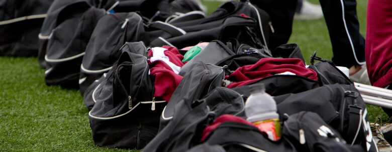 A row of open black sports duffel bags filled with clothing and gear sits on grass, with people standing nearby—perhaps preparing to load everything into a cargo van rental in Munster for their next adventure.